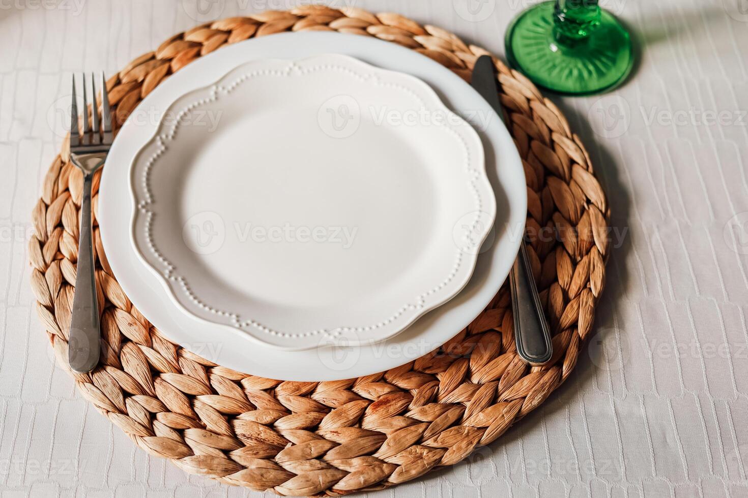 Elegant dining setup featuring a white plate on a woven placemat with silverware photo