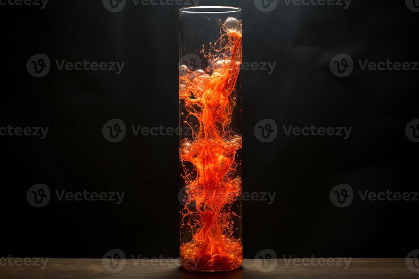 Orange ink spreading in water inside a glass cylinder on a dark background photo