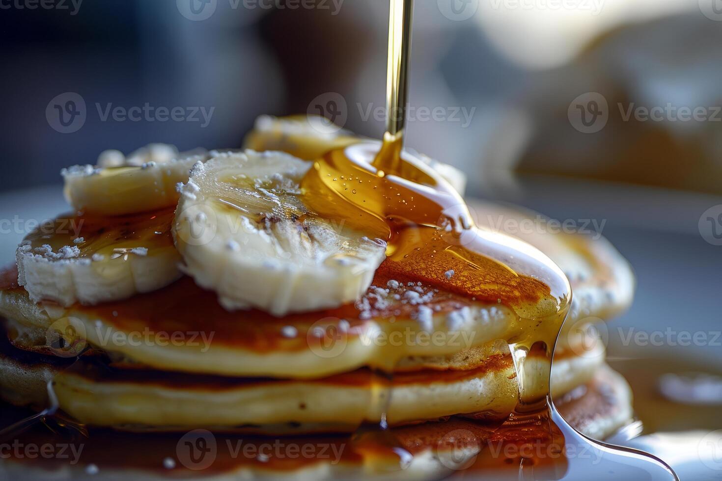 Pouring maple syrup on stack of pancakes with sliced banana and powdered sugar photo
