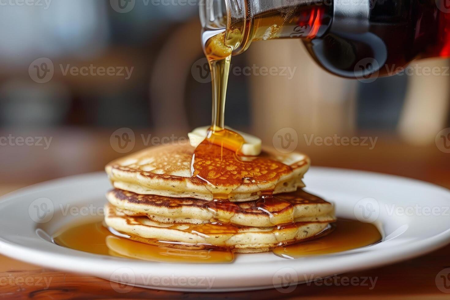 Pouring maple syrup on stack of pancakes with butter for breakfast photo