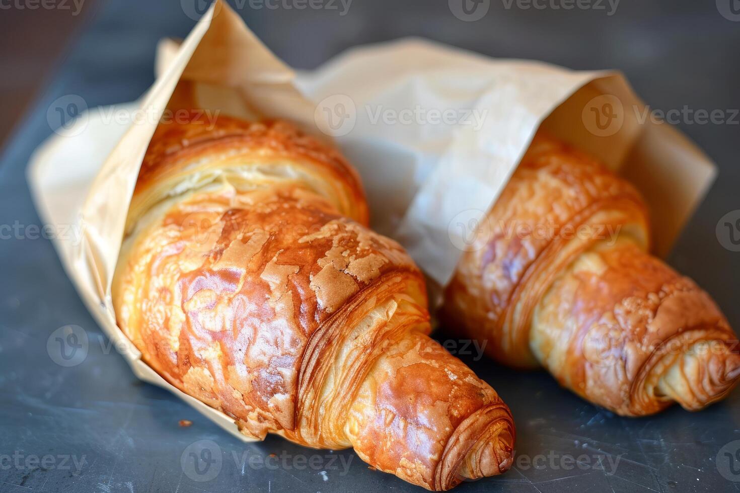Two freshly baked croissants wrapped in brown paper on dark surface photo