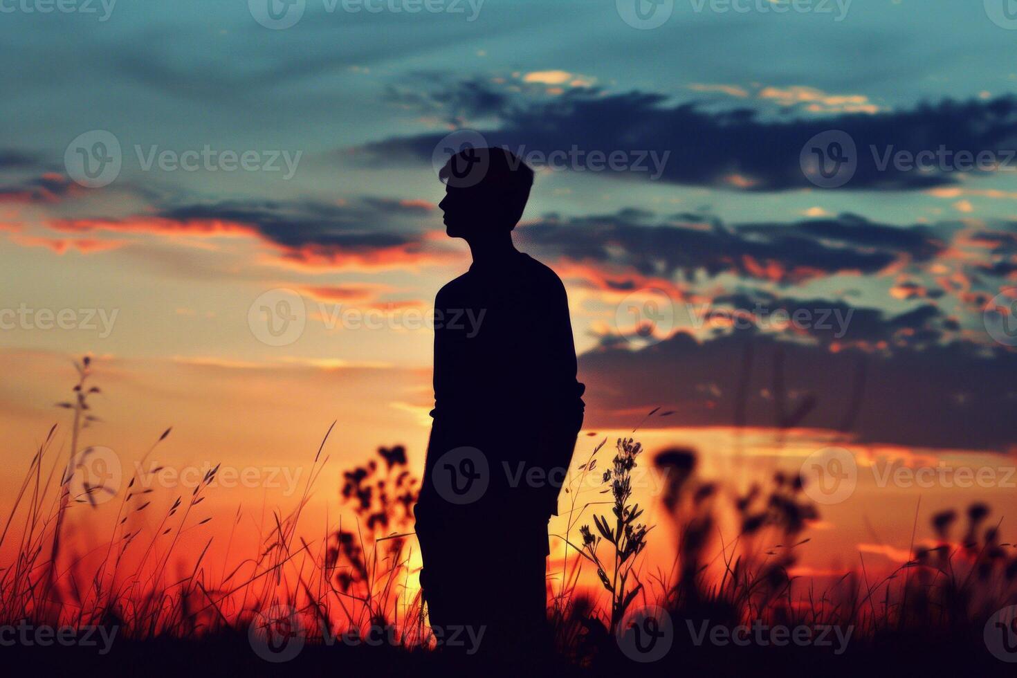Young man contemplating dramatic sunset in a field at twilight photo