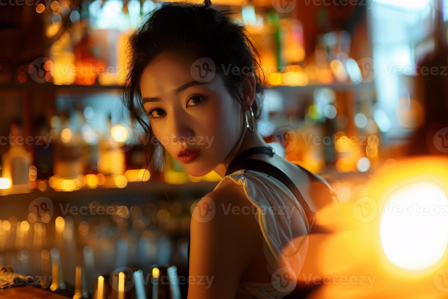 Bartender woman working at cocktail bar with blurred bottles in background photo