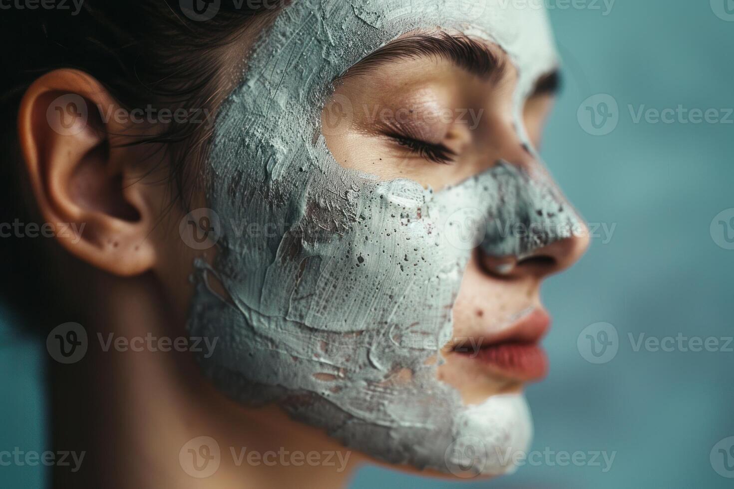 Young woman applying a purifying clay mask on her face for skin care photo