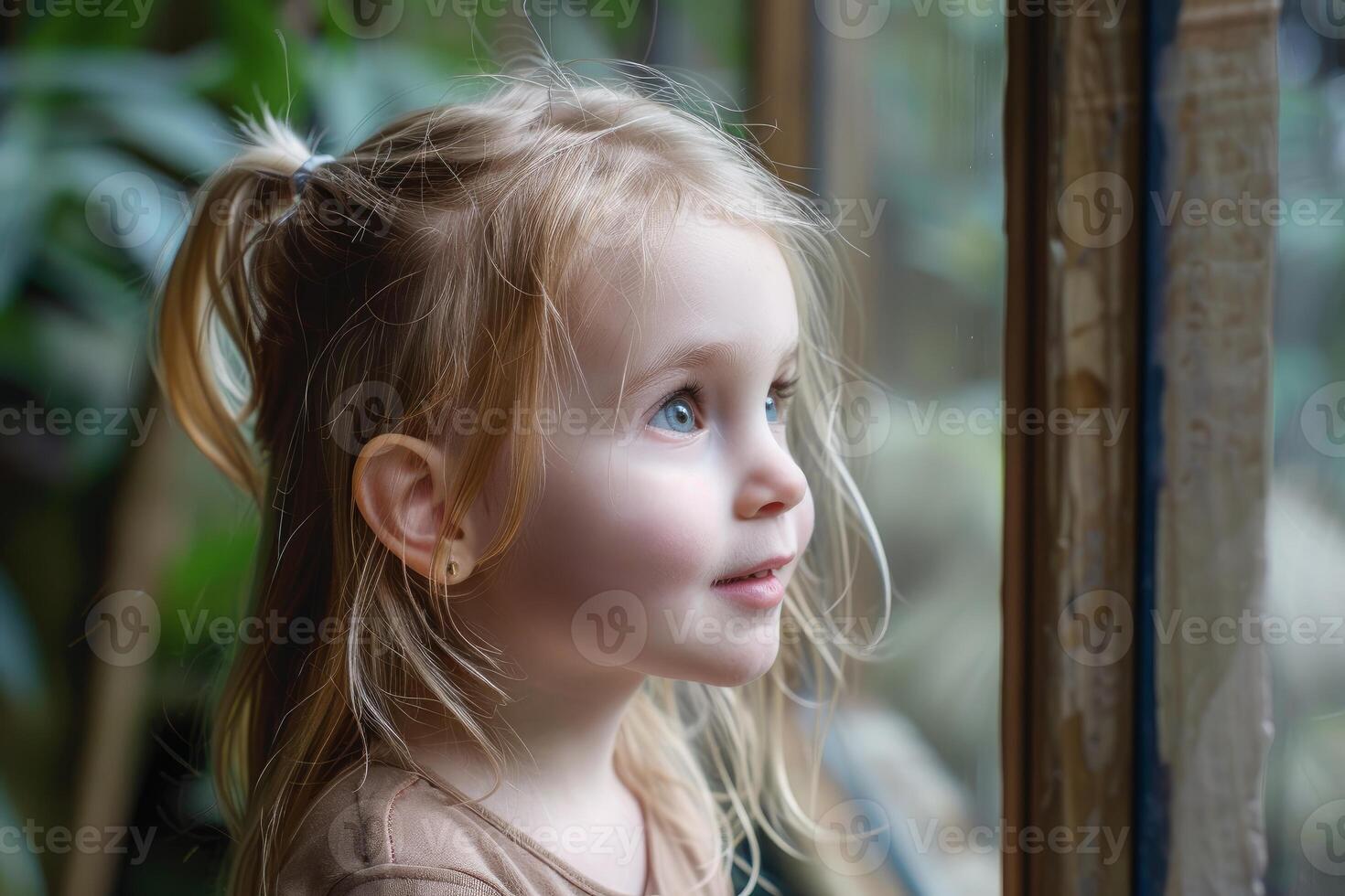 Little girl with pigtails observing something through the window photo