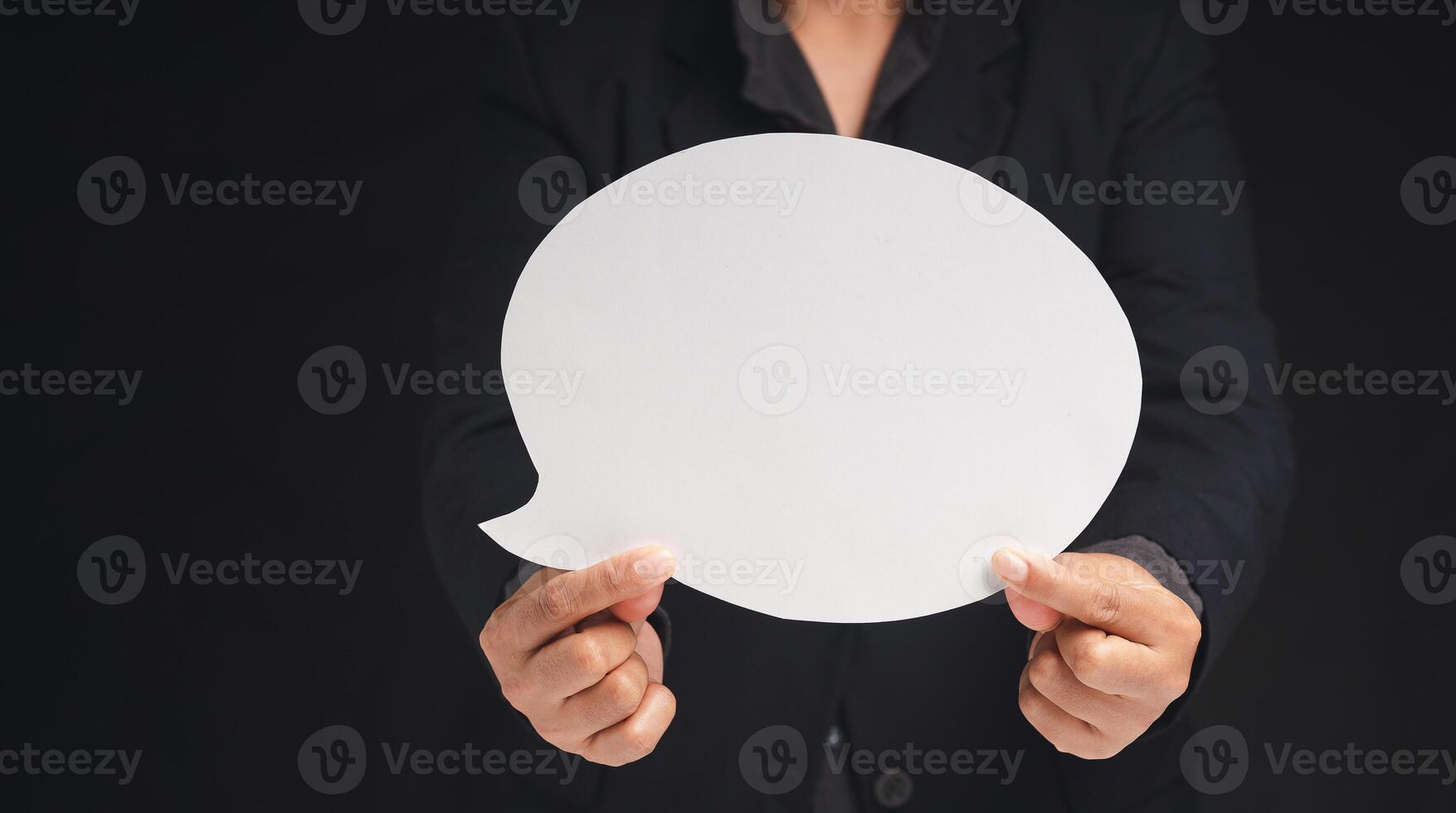 Close-up of a businessman holding a blank white speech bubble while standing on a black background. Space for text. photo