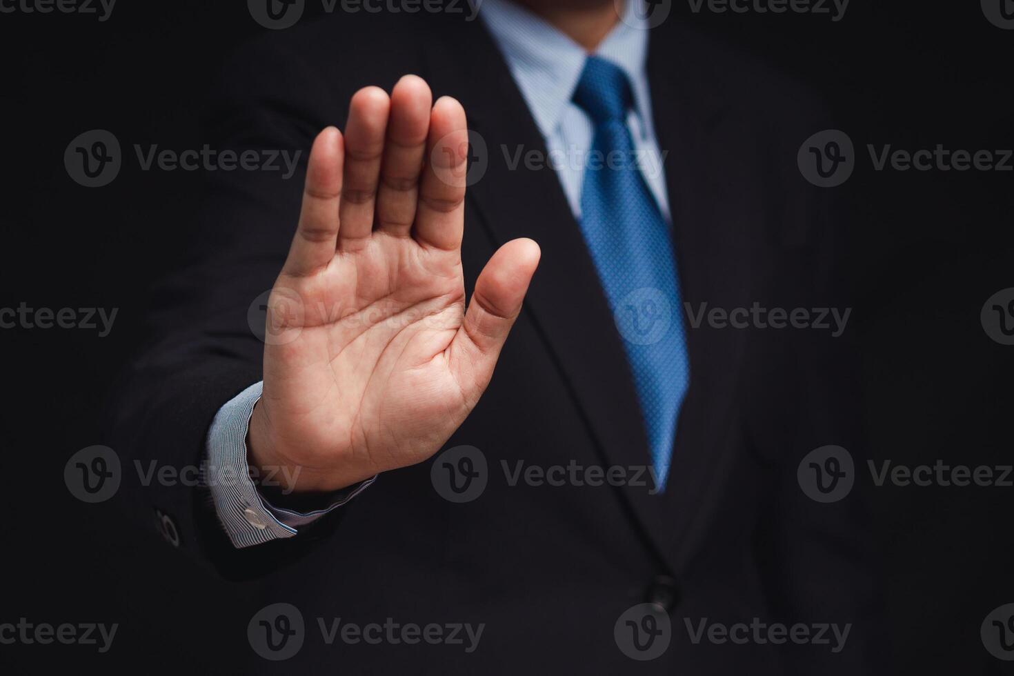 Businessman shows a stop gesture while standing on a black background photo