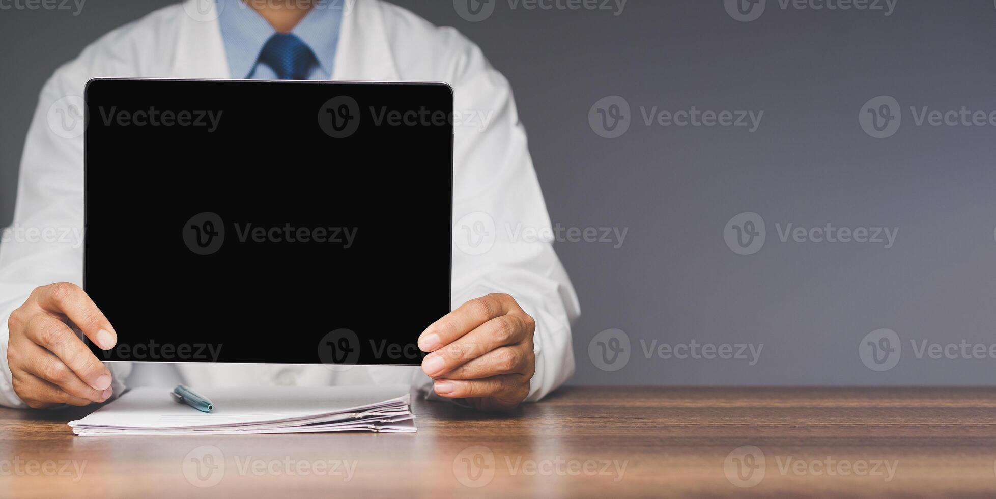 Close-up of a doctor holding a black blank screen tablet while sitting at the table in the hospital. photo