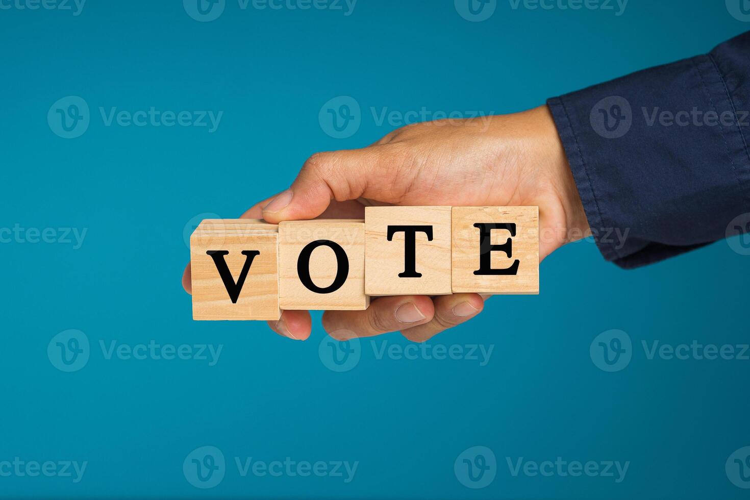 Close-up of hand holding wooden cubes with letters VOTE against a blue background photo