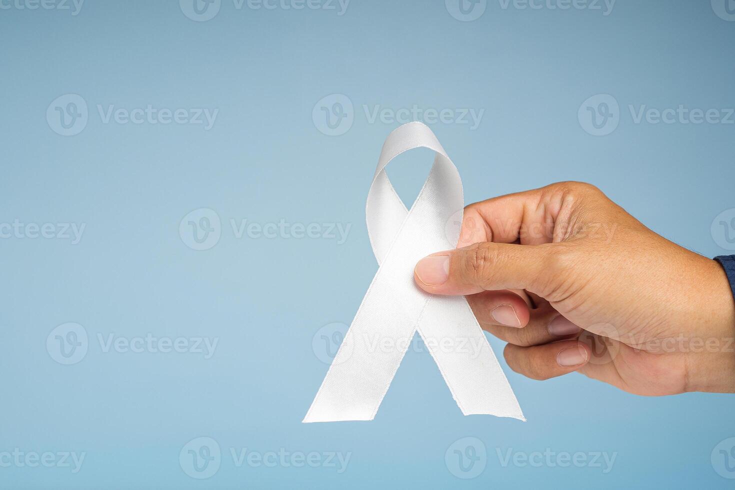 Hand holding a white ribbon symbol the fight lung cancer against on a blue background photo