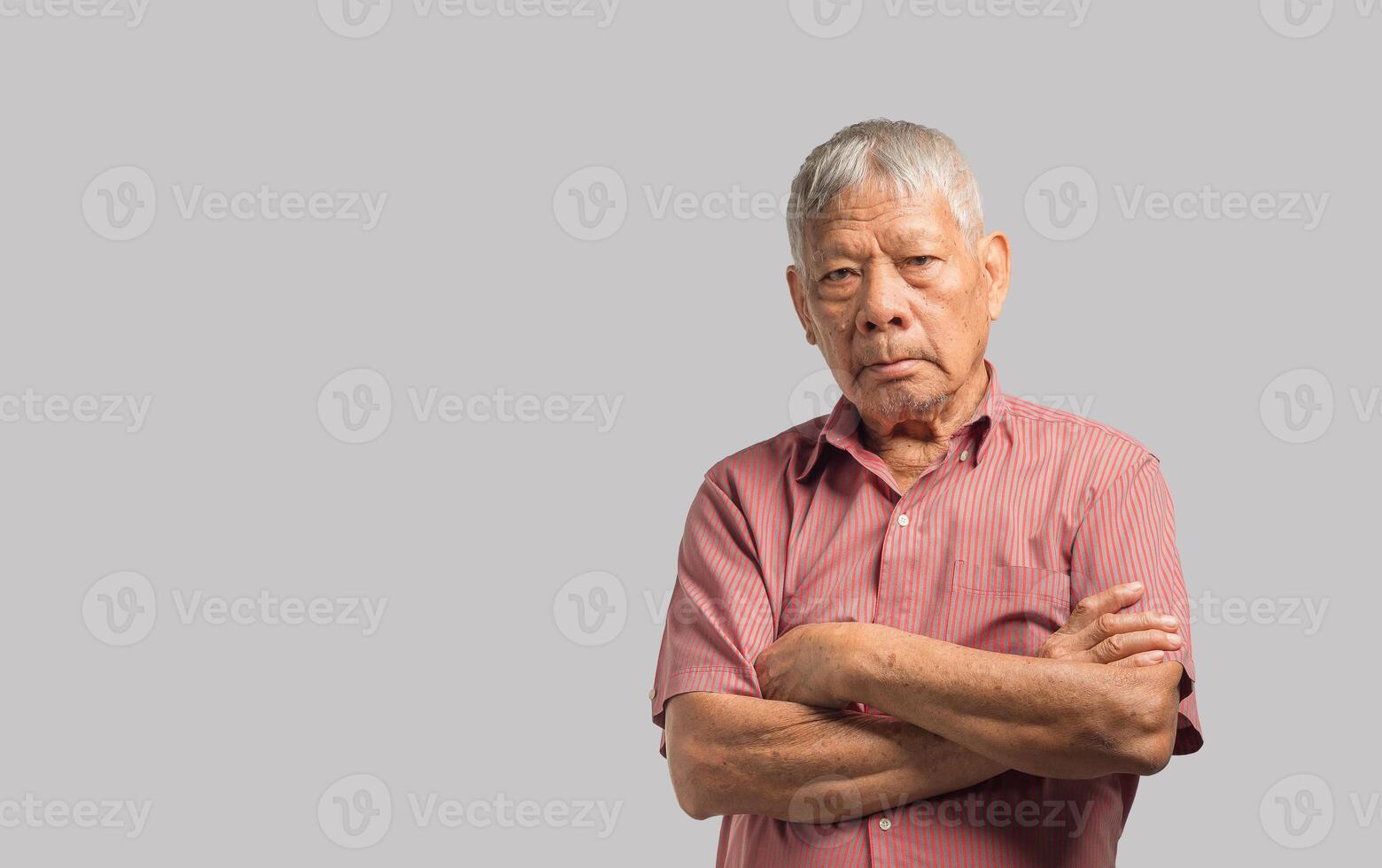 Senior man looking at the camera with a smile and arms crossed while standing on a gray background. Space for text. photo