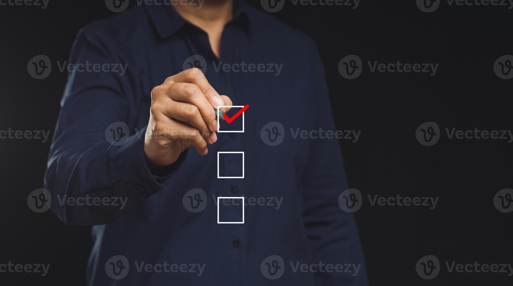 Businessman holding a pen and checking a mark on the boxes symbol is one of three options while standing on a black background photo
