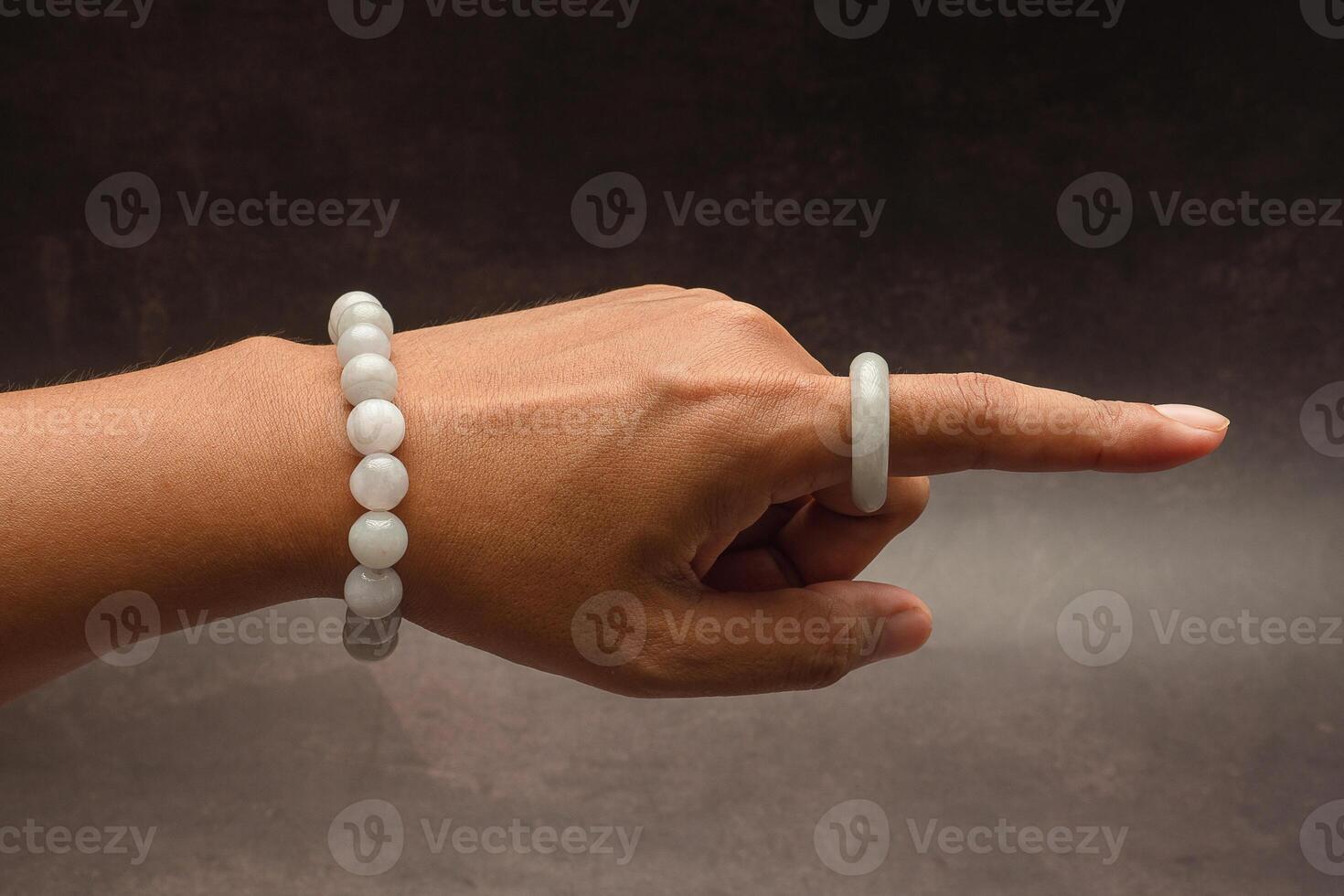 Jade bangle or bracelet on the wrist and a white jade ring on a finger against a black background photo