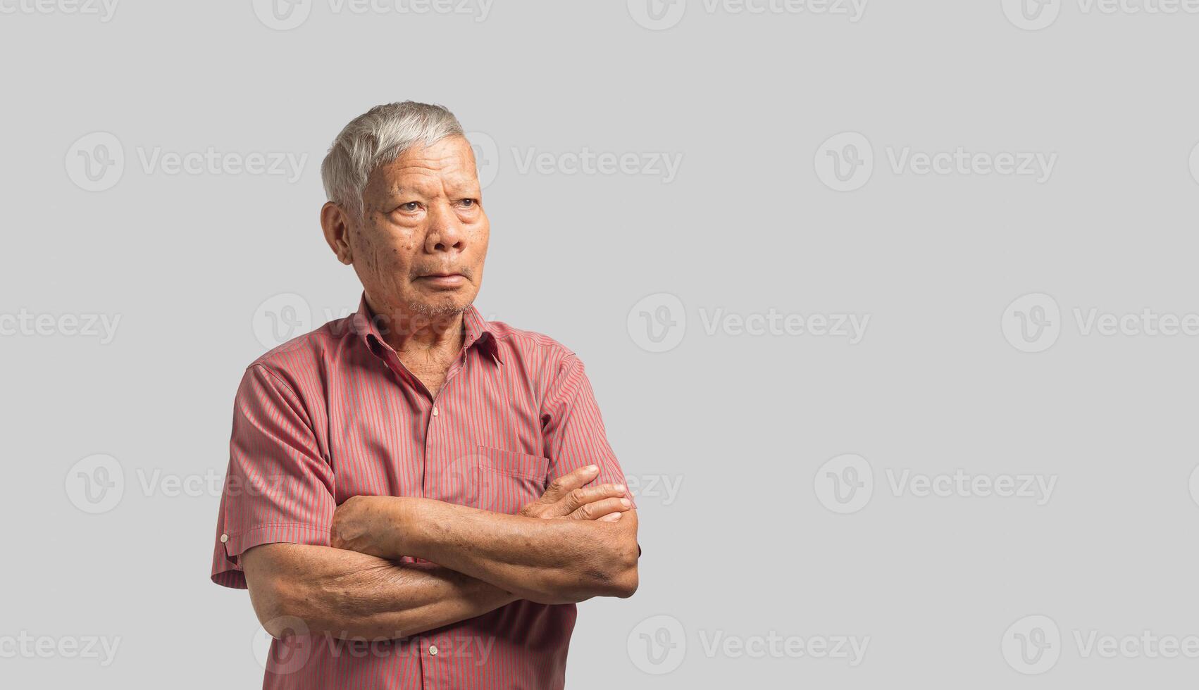 Portrait of a senior man in a shirt is looking away while standing arms crossed on a gray background. photo