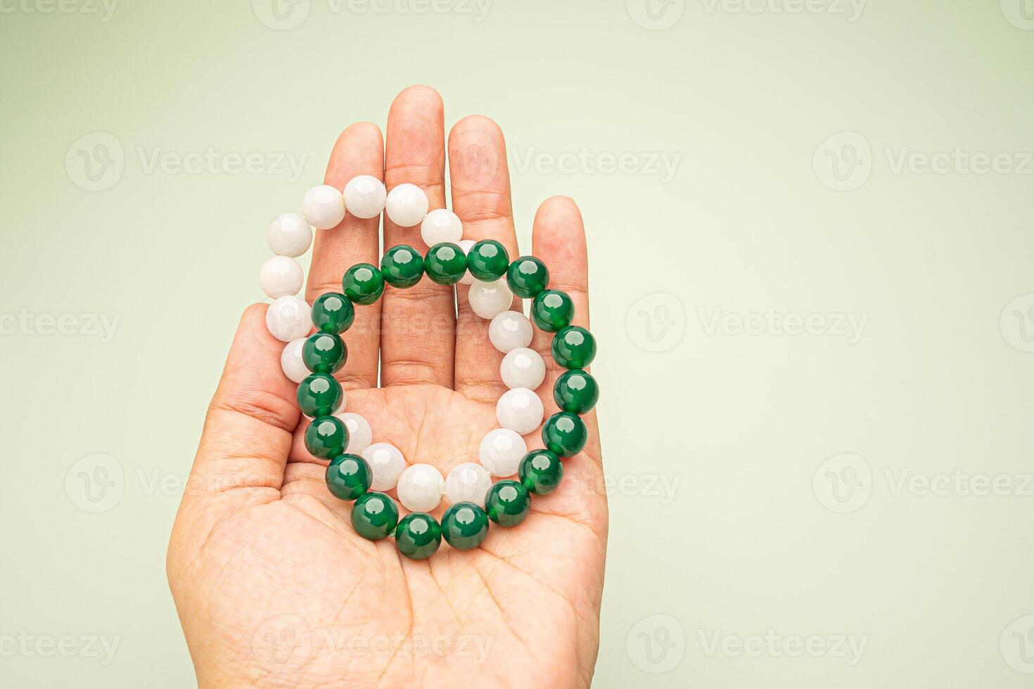 Two jade bangles or bracelets in hand against a green background. Space for text. photo