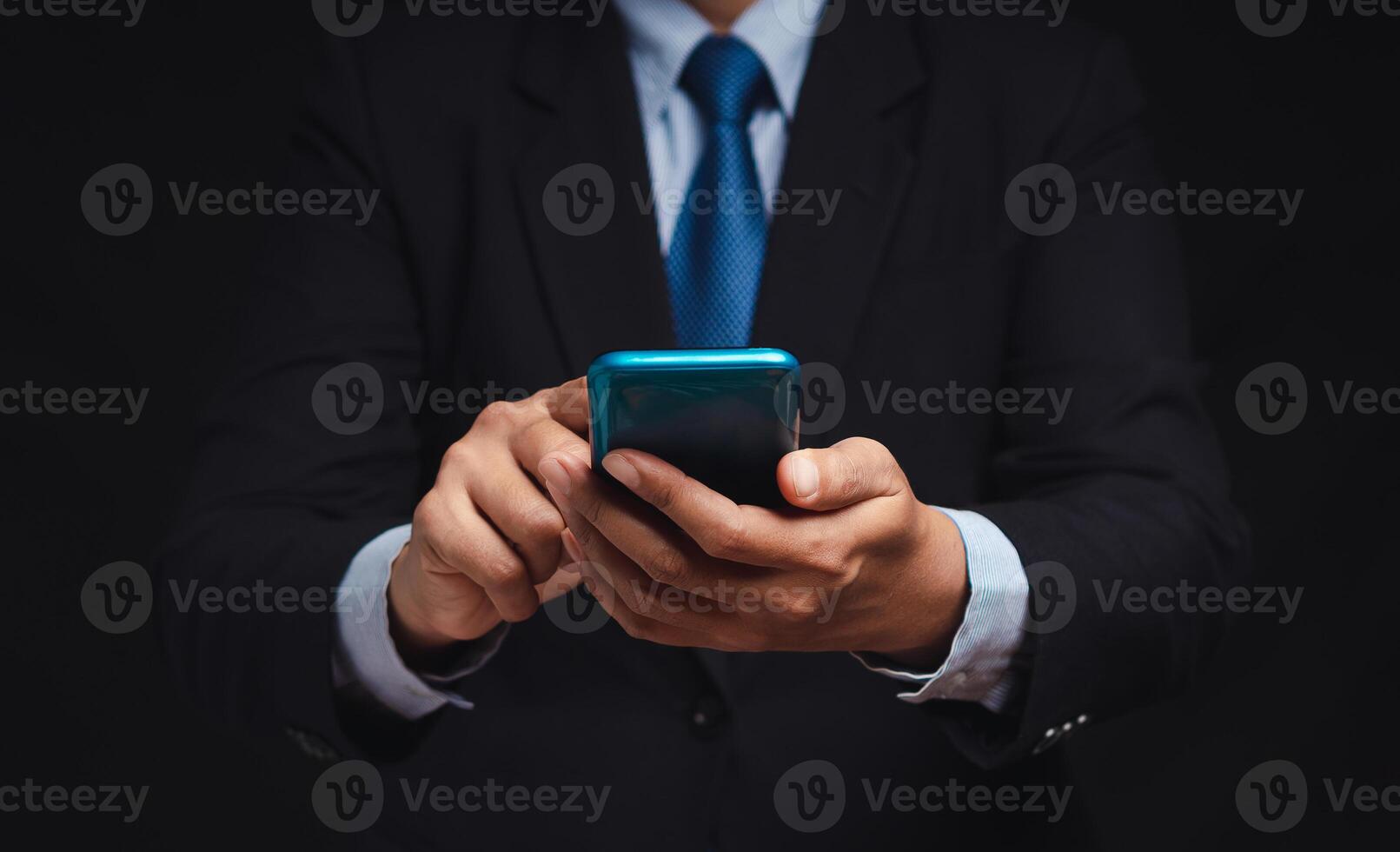 Businessman in a suit using a smartphone while standing on a black background photo