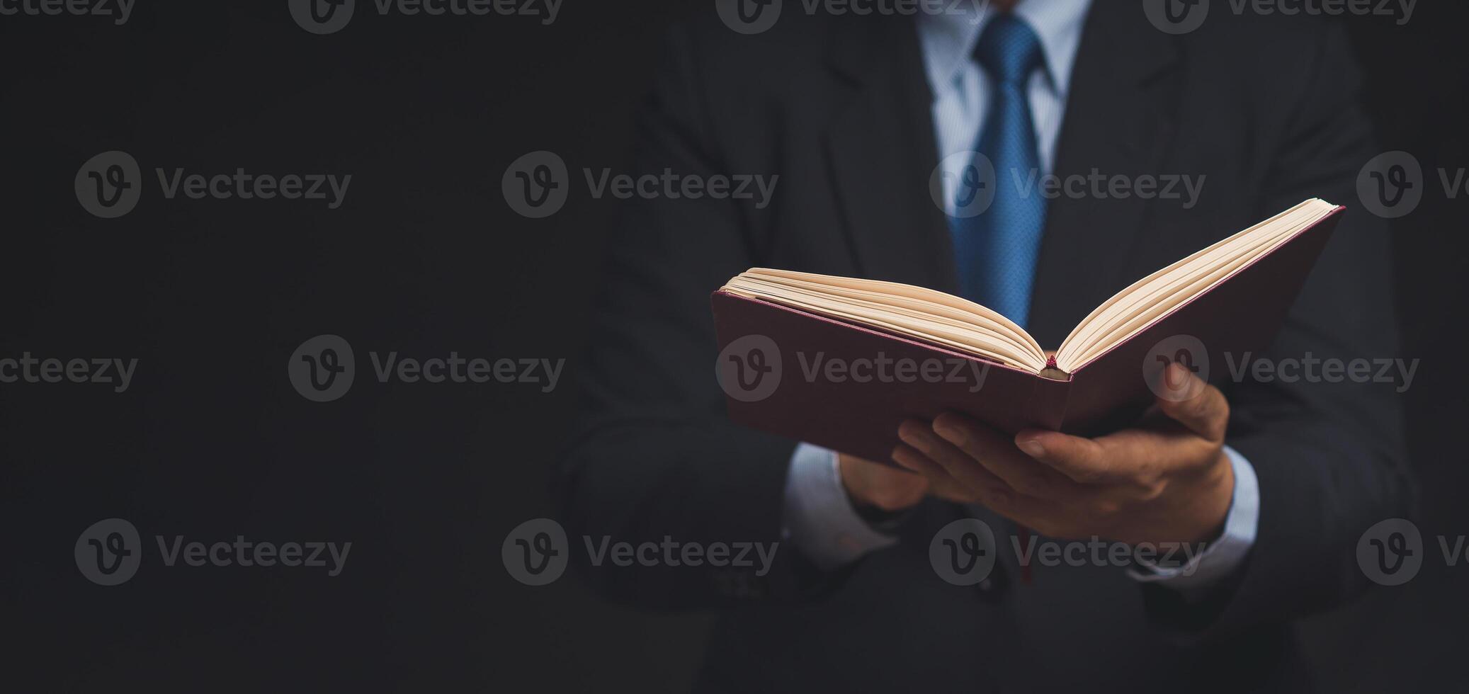 Businessman in a suit reading a book while standing on a black background photo