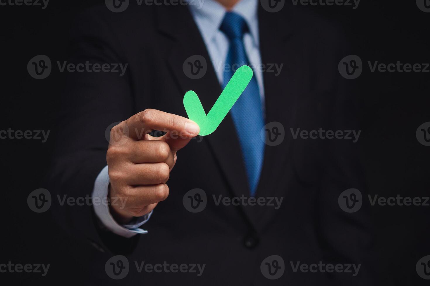 Businessman holding a green check mark symbol while standing on a black background photo