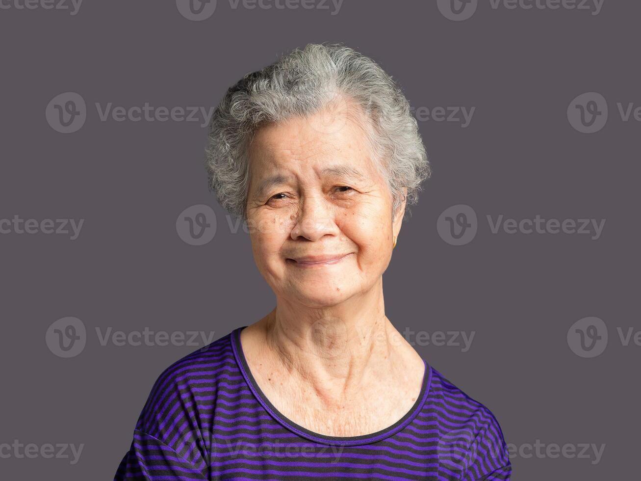Portrait of an elderly woman looking at the camera with a smile while standing on a gray background. photo