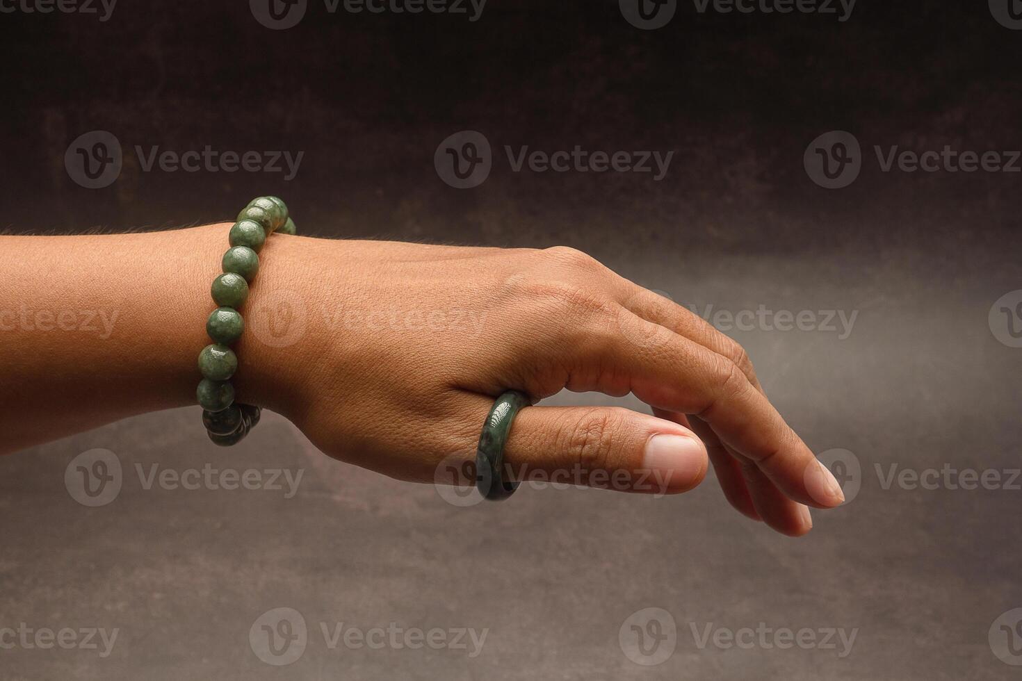 Close-up of a jade bangle or bracelet on the wrist and a green jade ring on a finger against a black background photo