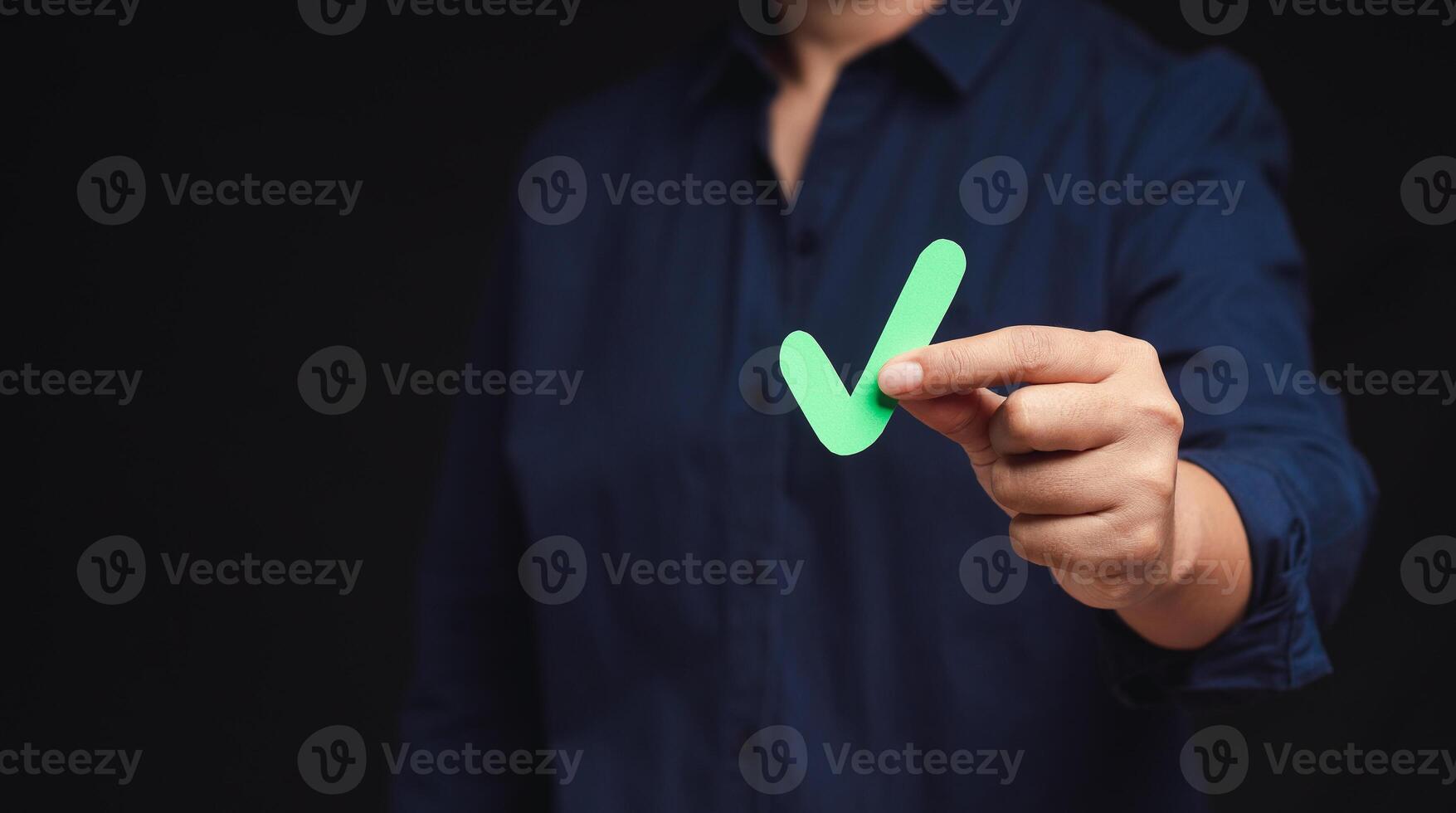 Close-up of hand holding a green check mark symbol while standing on a black background photo