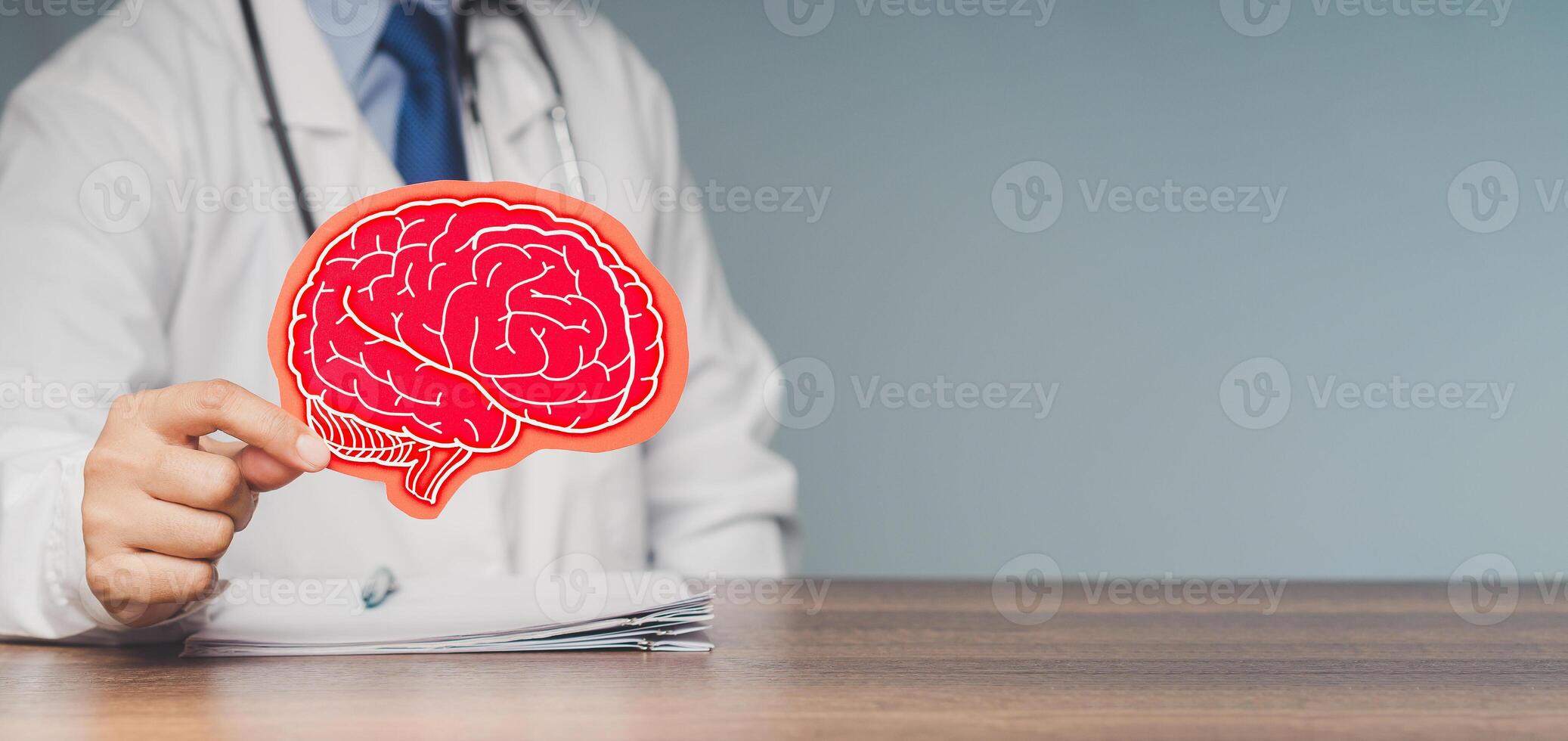 A doctor holding a brain symbol made from red paper while sitting at the table in the hospital photo