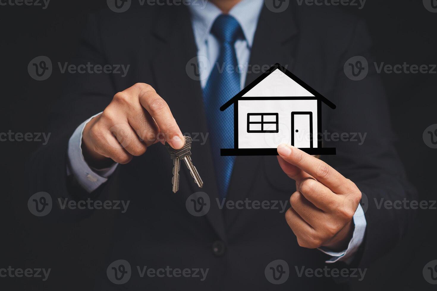 Business and real estate concept. A businessman in a suit holding keys and a mini paper house while standing in the office photo