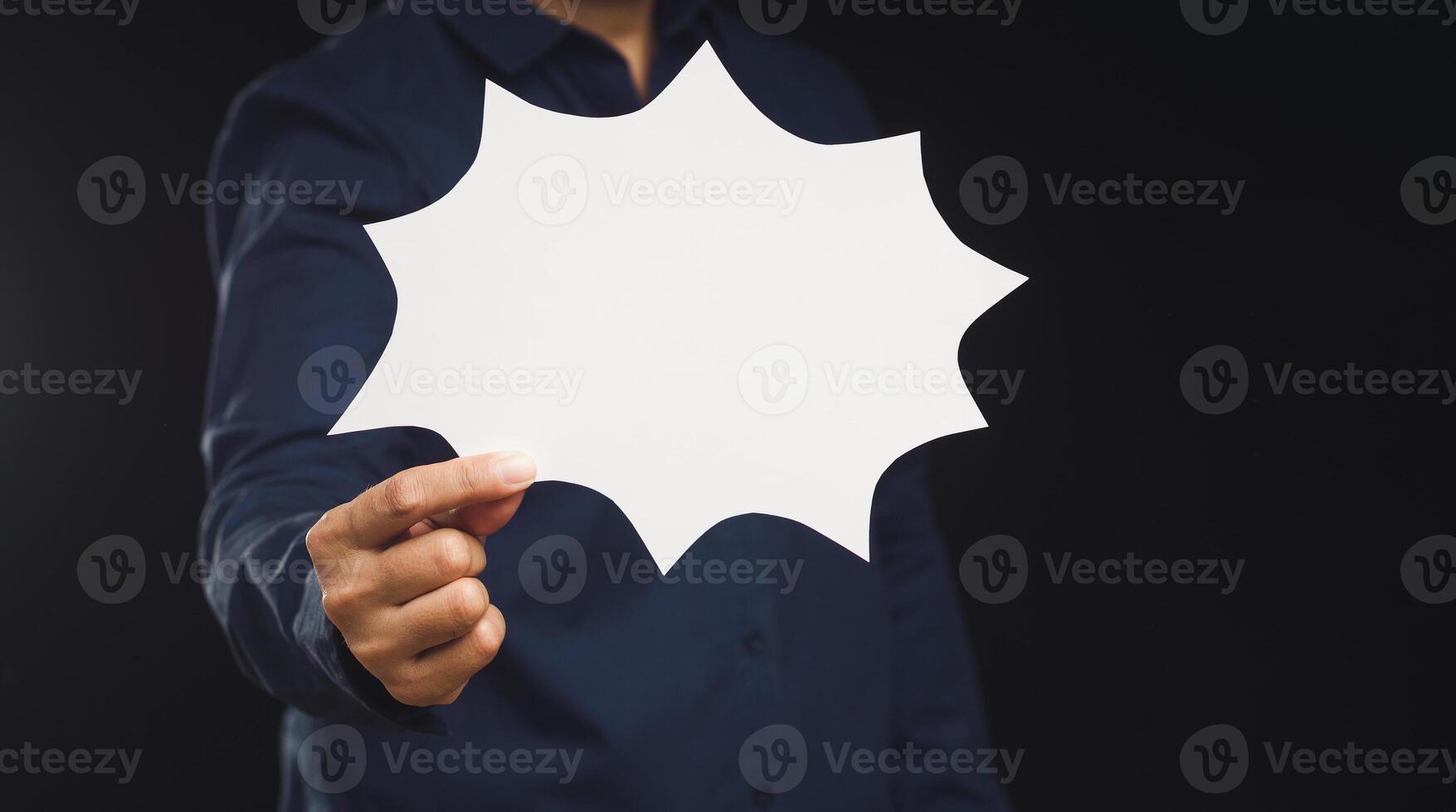 Businessman holding a blank white comic speech bubble while standing on a black background photo