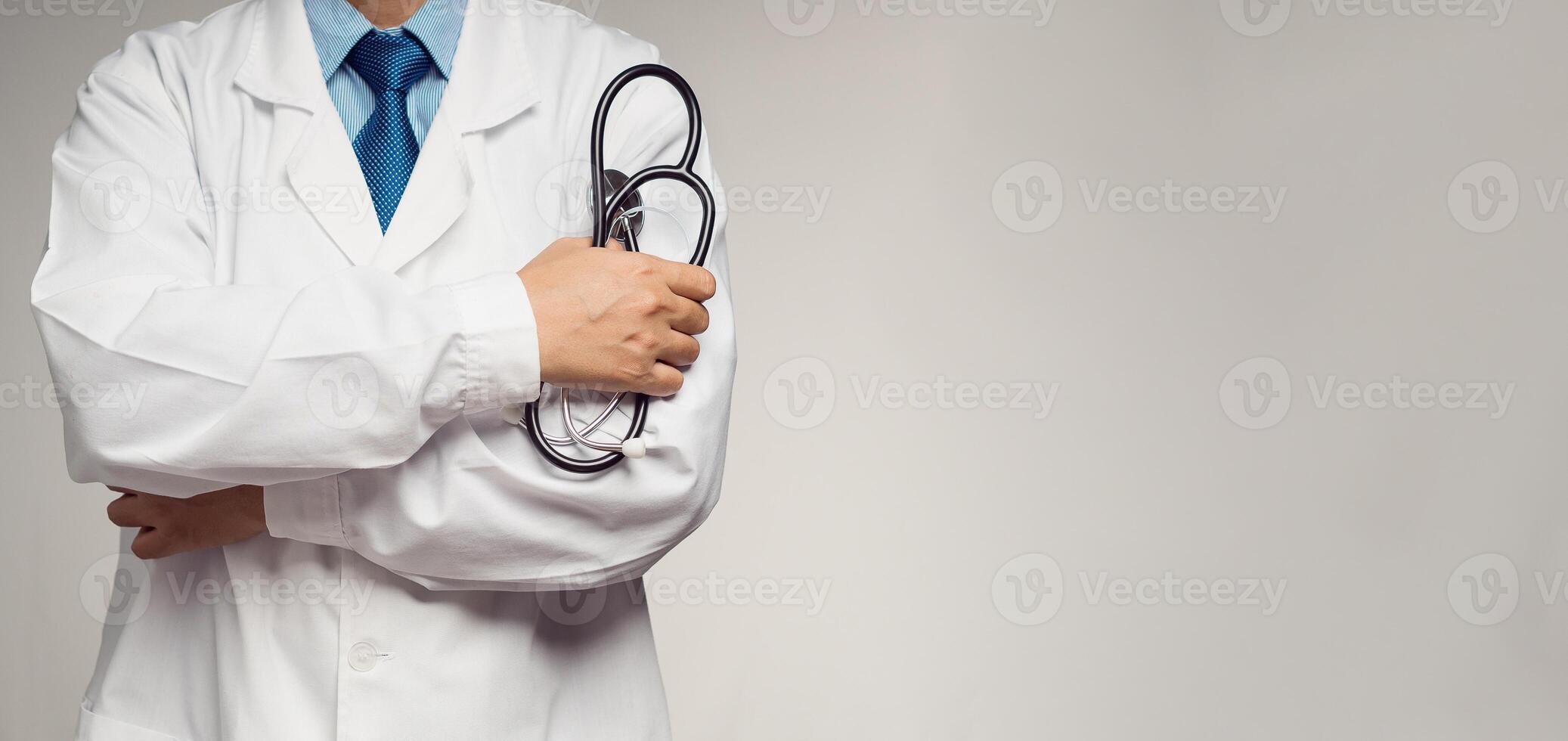 Doctor in uniform holding a stethoscope standing with arms crossed on a gray background photo