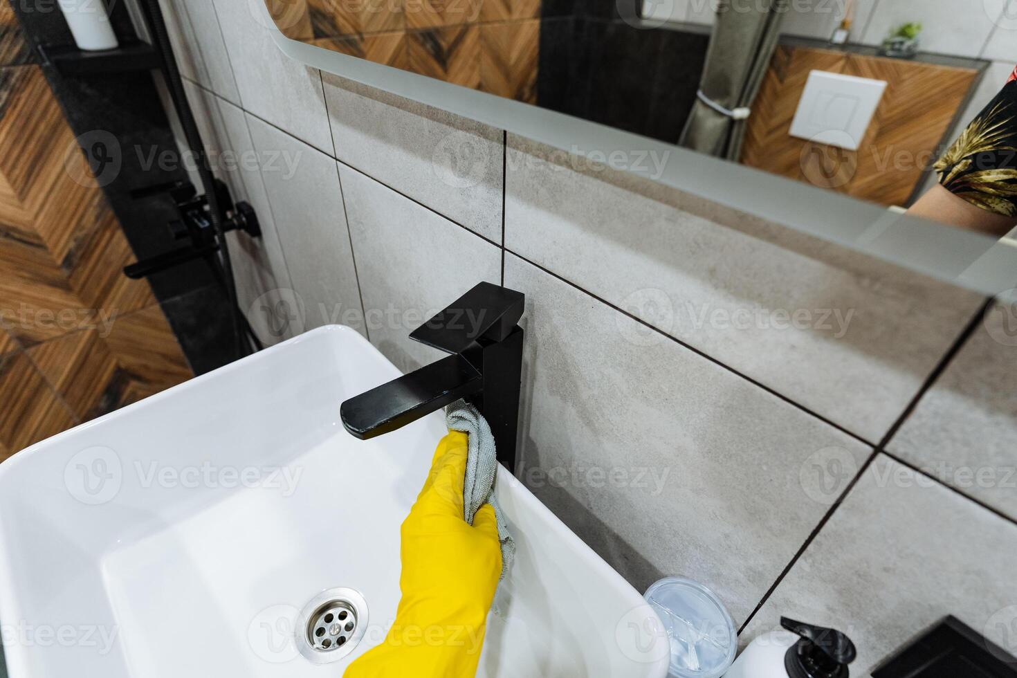 A person dressed in bright yellow rubber gloves is diligently cleaning a bathroom sink, ensuring that all areas are spotless and hygienic for future use and maintaining cleanliness photo