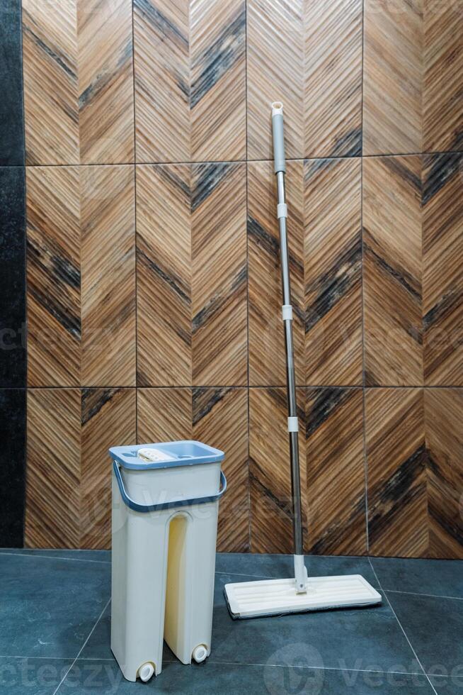A mop and a bucket filled to the brim with clear water rest neatly on the polished floor before a beautifully crafted wooden wall, which enhances the rooms rustic charm and warmth photo