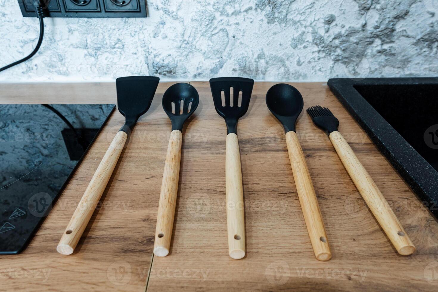 A beautifully arranged set of kitchen utensils featuring elegant wooden handles is neatly lined up on a rustic wooden counter, adding charm and functionality to the workspace photo