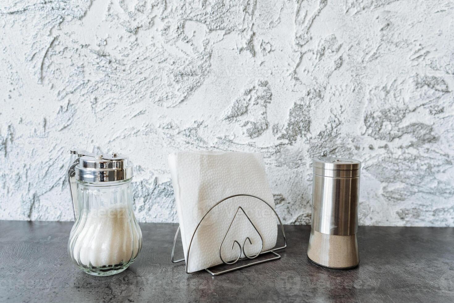 The table elegantly showcases a convenient napkin holder, stylish salt and pepper shakers, and fresh garlic, crafting a casual yet functional atmosphere for dining or meal preparation photo