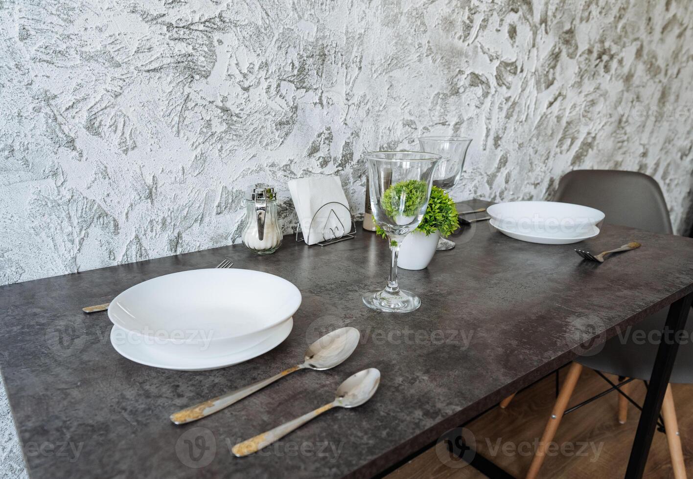 A beautifully set dining table adorned with dishes, utensils, glasses, and a lovely plant arrangement placed on it, creating an inviting atmosphere for meals and gatherings photo