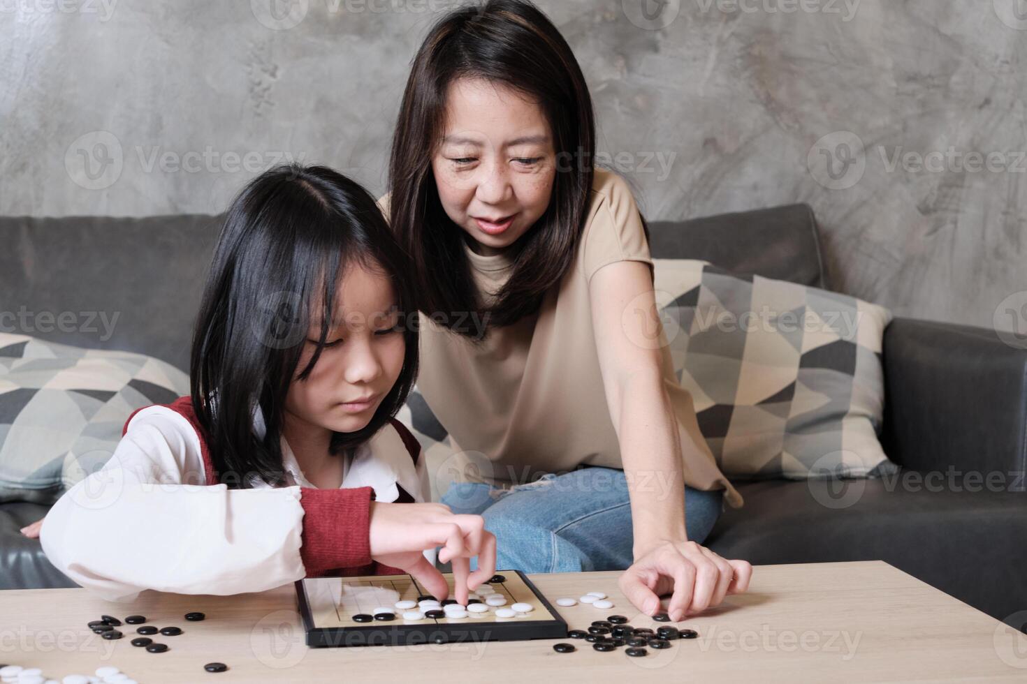 Single mother, and child concentrate playing Go, checkers board game on table in home living room together with fun and cheerful, happy weekend relaxing hobby of Asian family. photo