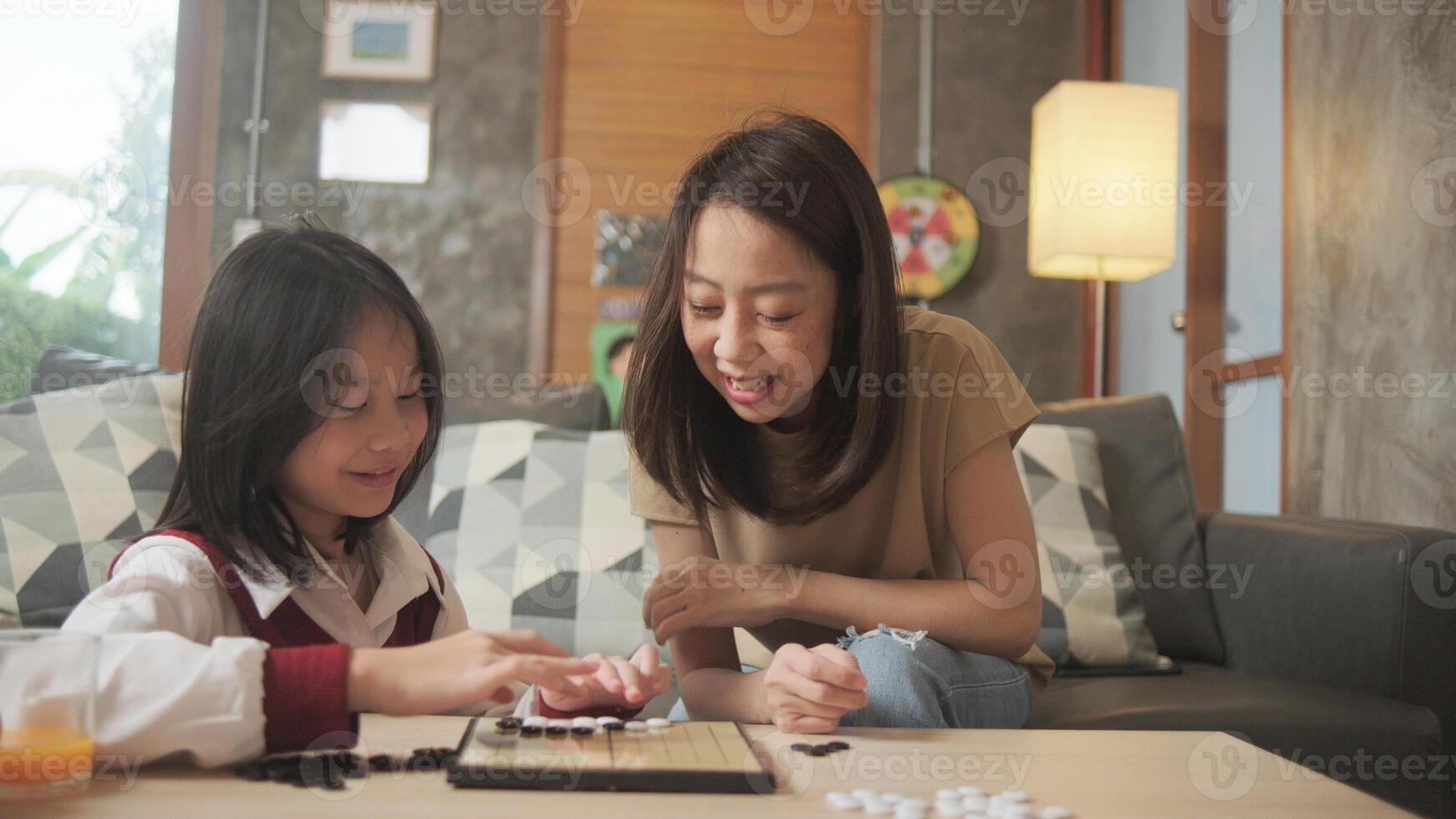 Asian family, mum, and kid fun playing checkers board game-GO on table in home living room together with love and cheerful, happy weekend relaxing hobby of child and parent, concentrate and compete. photo