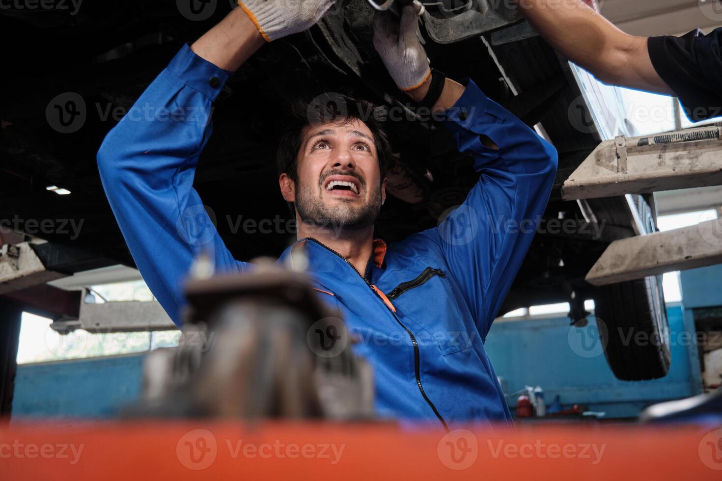 Latino male mechanic worker checks and fixes automotive wheels and maintains car suspensions in garage station, and undercarriage technician engineering service jobs in vehicle transport industry. photo