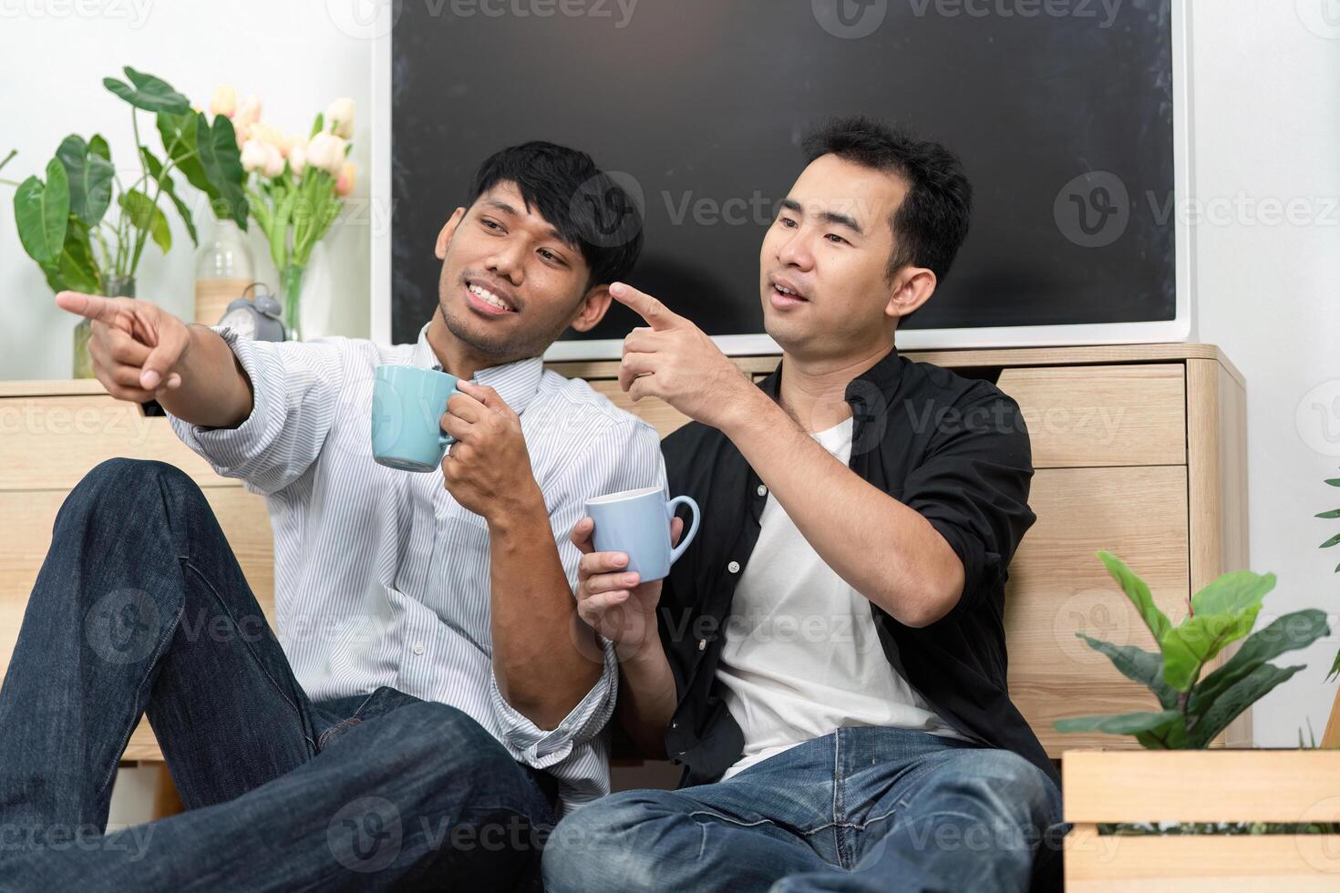 Connection and LGBT Love. Two men sharing a joyful moment over coffee, pointing and laughing together in a cozy living room. photo
