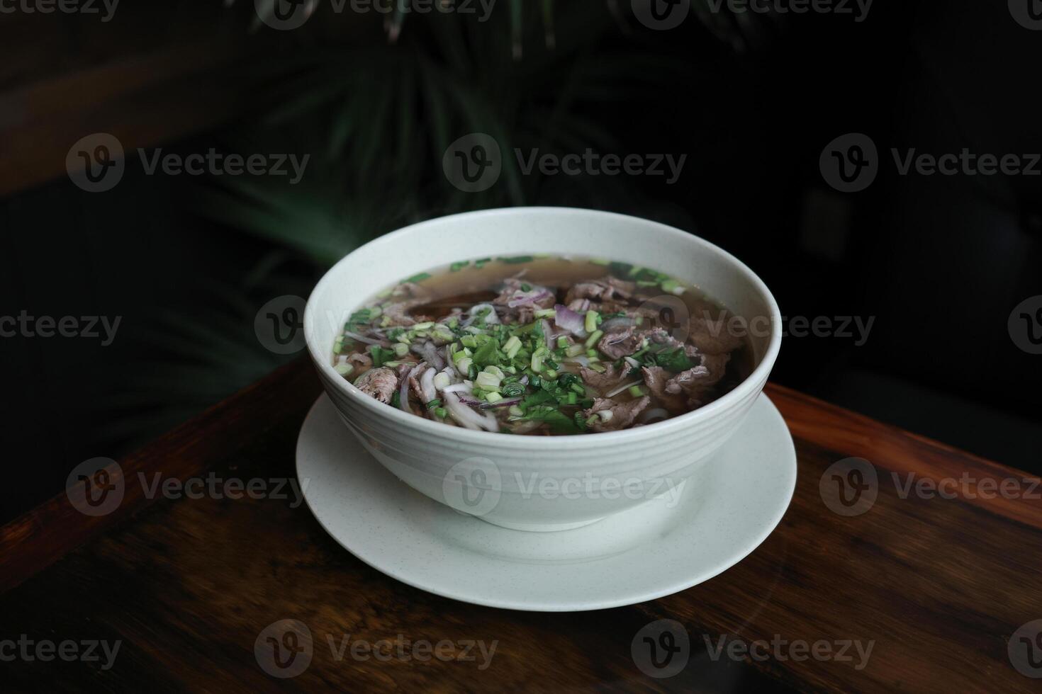 Traditional Vietnamese pho soup with beef slices served in a white ceramic bowl decorated with cilantro and green onion. Concept of authentic Asian cuisine, healthy food and comforting homemade meals. photo