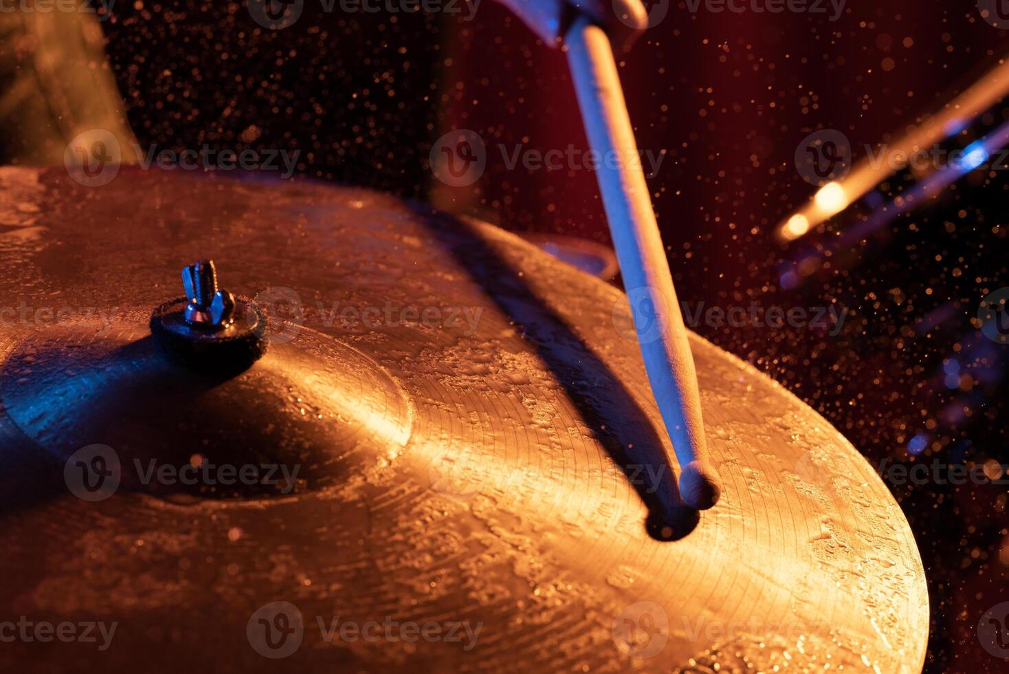 Drum sticks hitting snare drum with splashing water on dark background with orange and blue studio lighting. Dynamic scene. photo