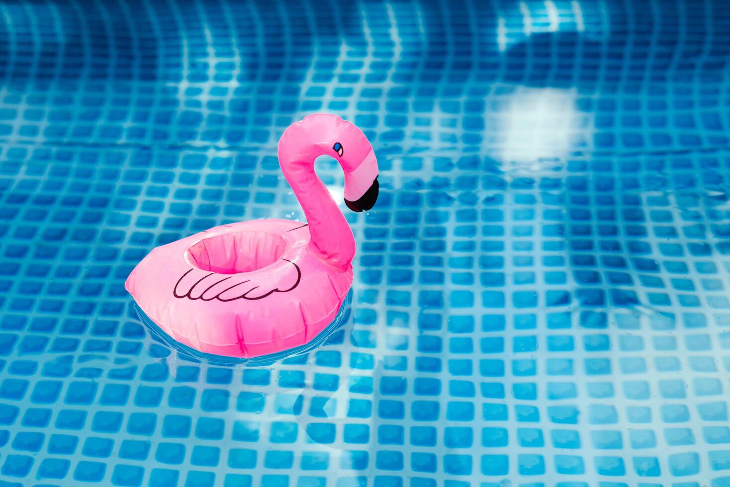 Inflatable pink flamingo floating in a clear blue swimming pool. photo