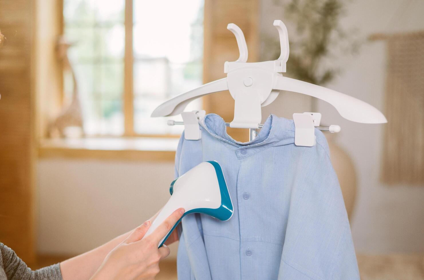 Using steaming iron to ironing shirt in home. Doing stream vapor iron for press clothes in hand close up photo