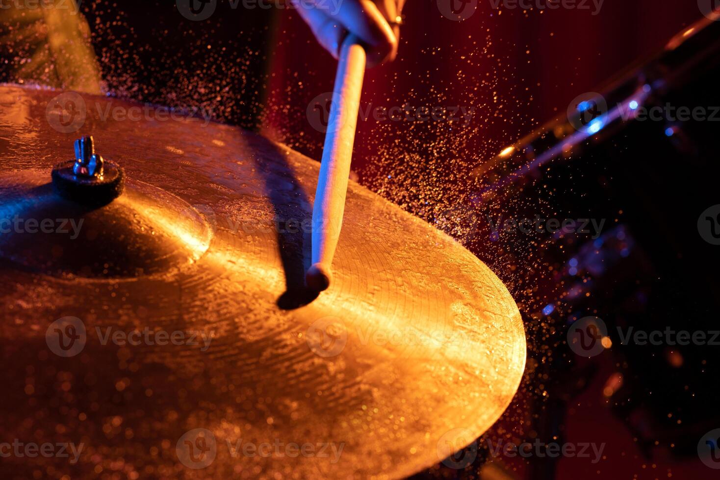 Drum sticks hitting snare drum with splashing water on dark background with orange and blue studio lighting. photo