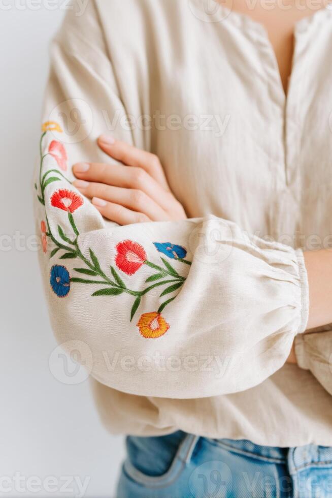 Close-up of a person wearing a light-colored embroidered blouse with floral designs on the sleeves, showcasing intricate craftsmanship and a relaxed, casual style photo