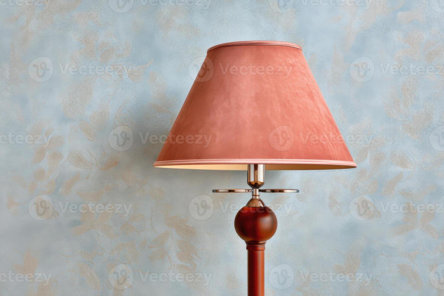 Elegant table lamp with a soft pink shade stands against a textured blue wall, creating a warm and inviting atmosphere in a cozy interior setting with copy space photo