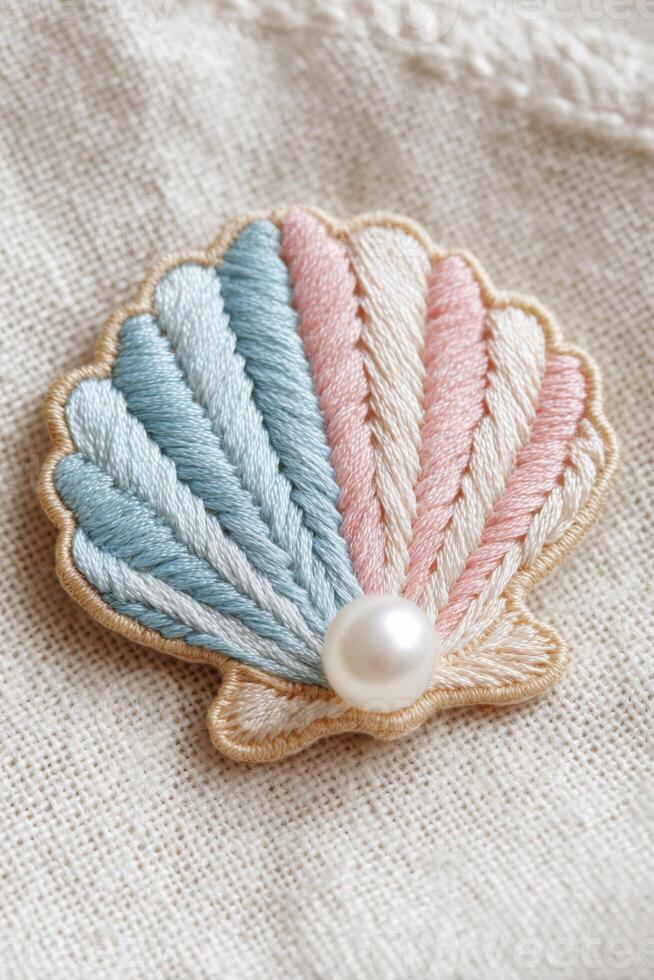 Embroidered shell patch featuring pastel colors of blue, pink, and cream, adorned with a pearl, showcasing intricate stitching on a textured fabric background photo