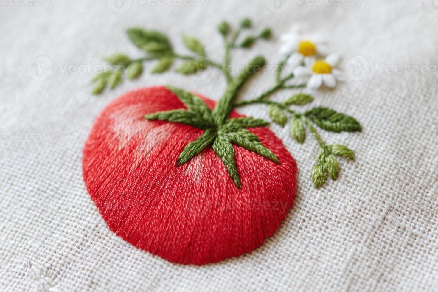 Embroidered red tomato with green leaves and white flowers on a textured fabric background, showcasing intricate stitching and vibrant colors in a decorative design photo