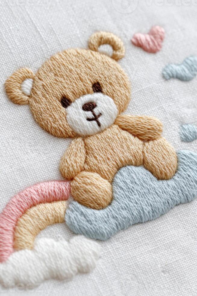 Cute teddy bear embroidered on fabric, sitting on a fluffy cloud with a rainbow, surrounded by pastel hearts, creating a whimsical and playful atmosphere for children's decor photo