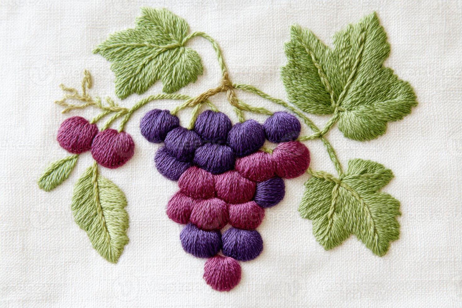 Embroidered grape cluster with vibrant purple and red threads, surrounded by green leaves, showcasing intricate textile art and craftsmanship in a decorative design photo