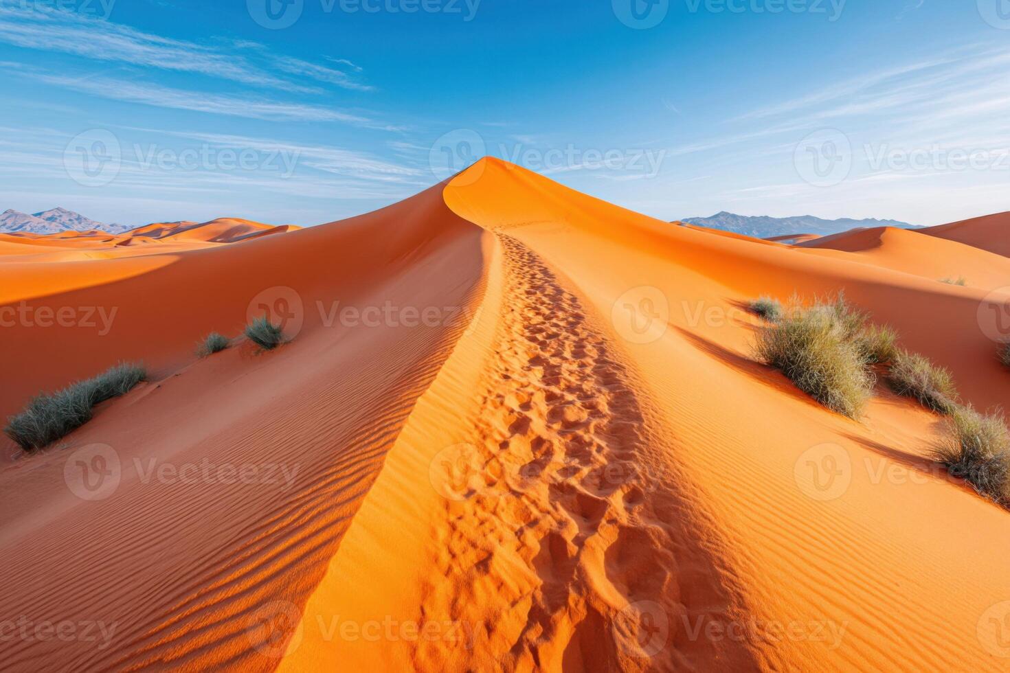 Majestic Moroccan desert landscape featuring vibrant orange sand dunes, a winding path through the dunes, and a clear blue sky creating a serene and tranquil atmosphere photo